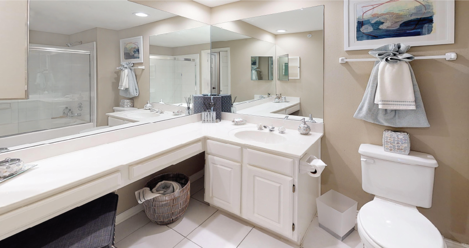 Spacious bathroom with oval soaking tub with glass enclosure, cultured marble vanity, glass shower, and built-in vanity at Tuscany Park Apartments in Houston.