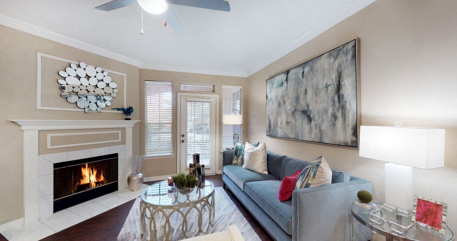 Spacious living room with wood-burning fireplace with glass doors, ceiling fan, French door and 9-foot ceiling at Tuscany Park Apartments in Houston.