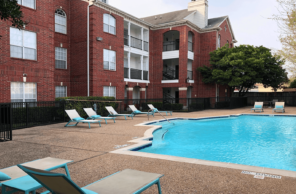 Luxury swimming pool with spacious sundeck, beautiful landscaping, and poolside lounge seating at Tuscany Park Apartments in Houston.
