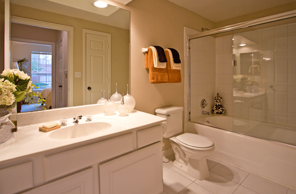Spacious bathroom with oval soaking tub with glass enclosure, cultured marble vanity, and glass shower at Tuscany Park Apartments in Houston.