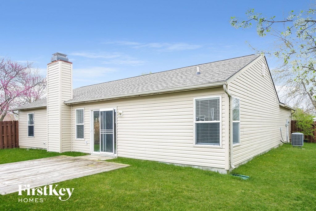 the backyard of a white house with a wooden deck