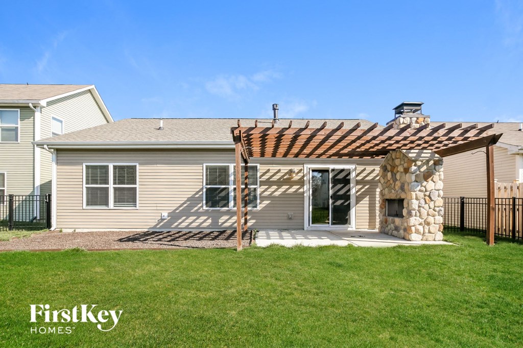 a patio with a stone wall and a pergola in front of a house