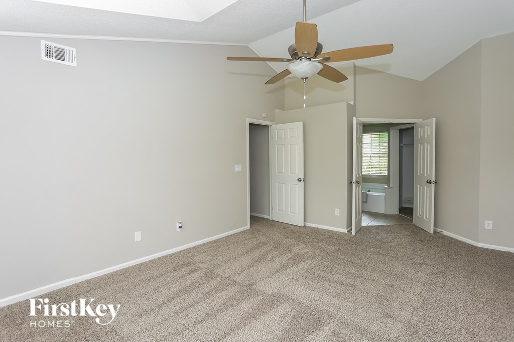 an empty living room with a ceiling fan and a door to a bathroom