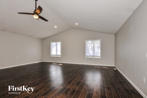 A spacious room with wooden floors and two windows.
