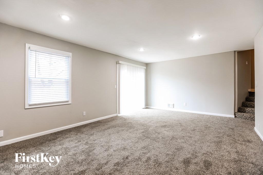 A spacious room with a carpeted floor and a window with blinds.