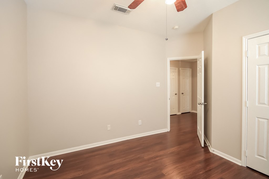 a bedroom with white walls and wood flooring and a door to a hallway