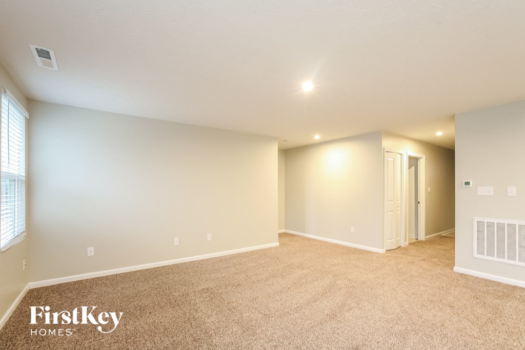 A spacious room with a carpeted floor and a window on the left side.