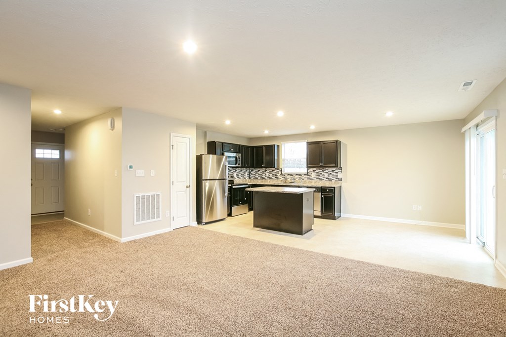 A spacious living room with a kitchenette in the background.