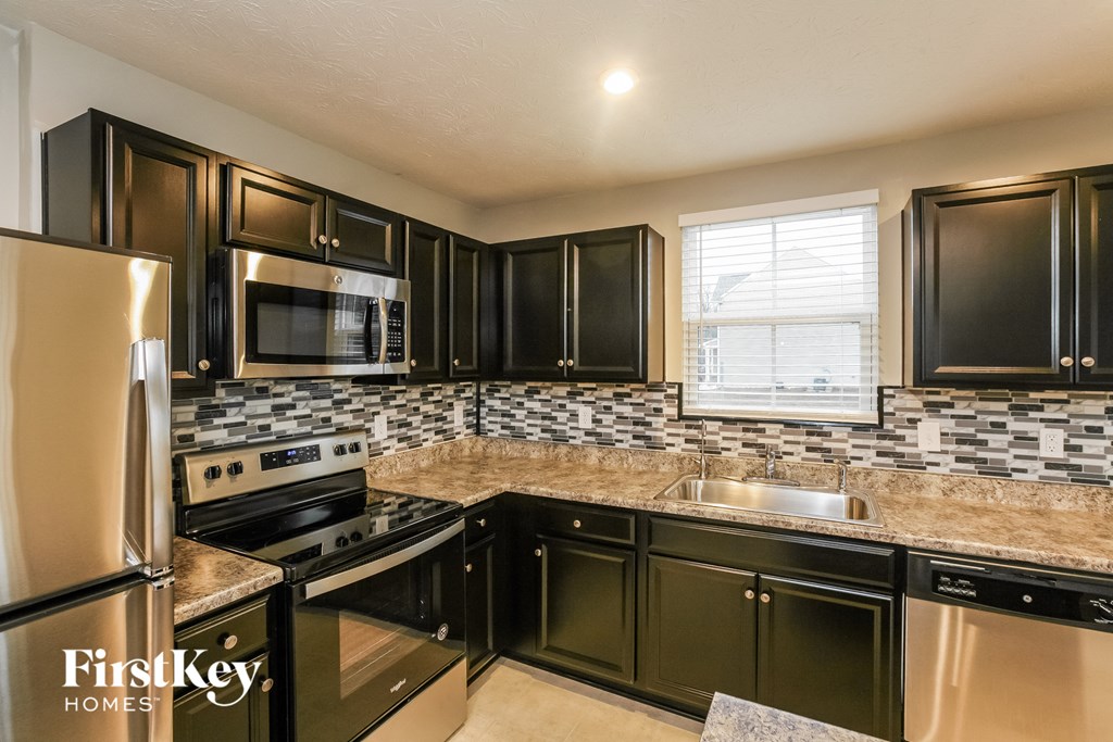 A kitchen with black cabinets and a stainless steel refrigerator.