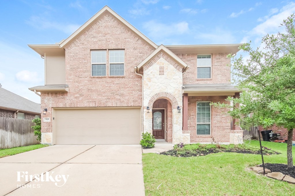 A brick house with a garage door and a tree in front.