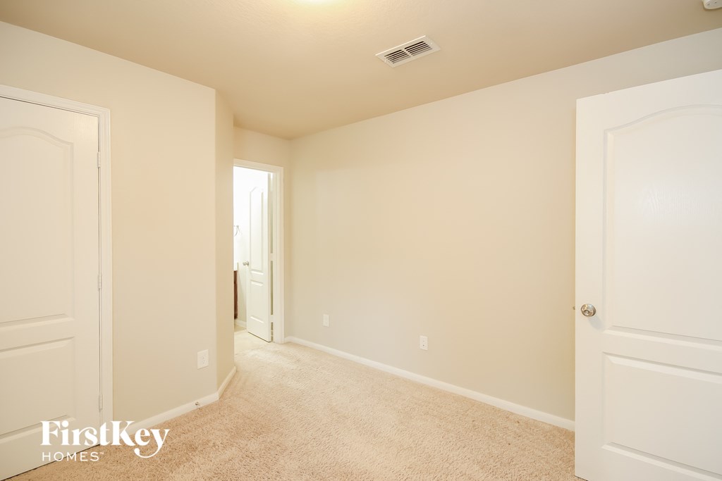 A white bedroom with a carpet floor and a door on the left.
