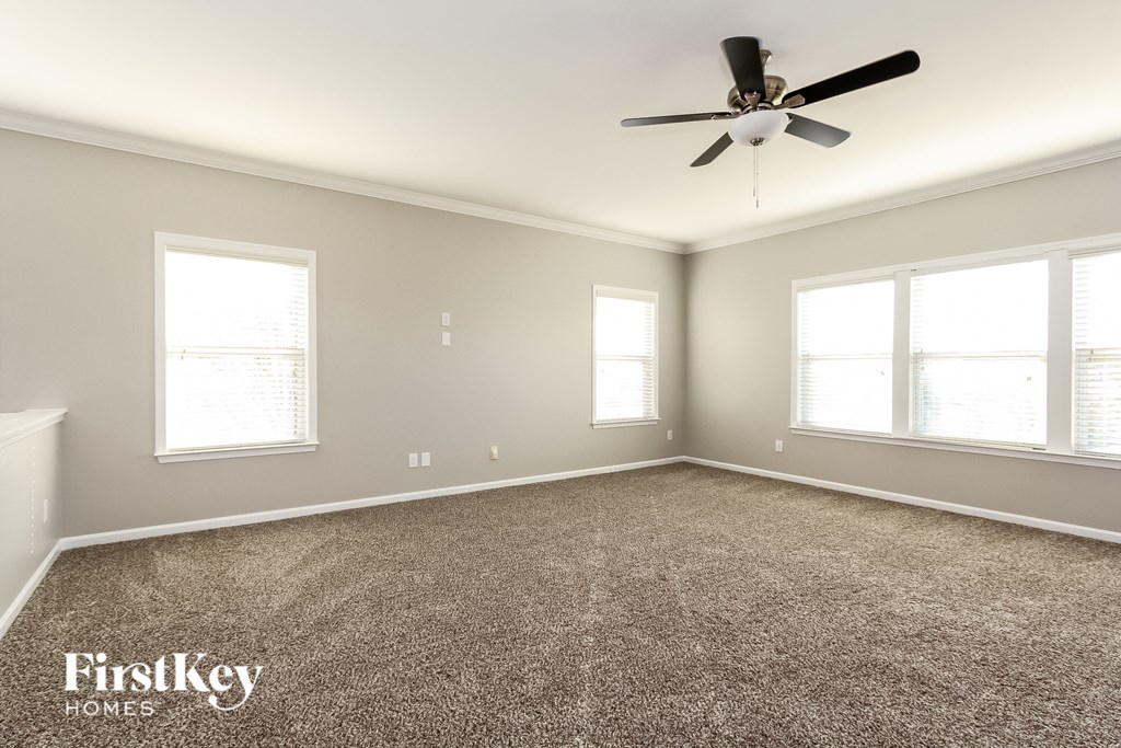 a carpeted living room with a ceiling fan and three windows