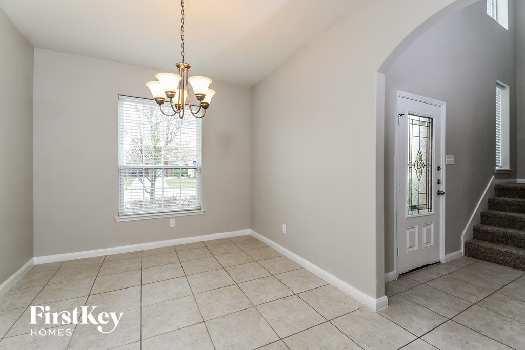 A room with a chandelier, a window with blinds, and a staircase.