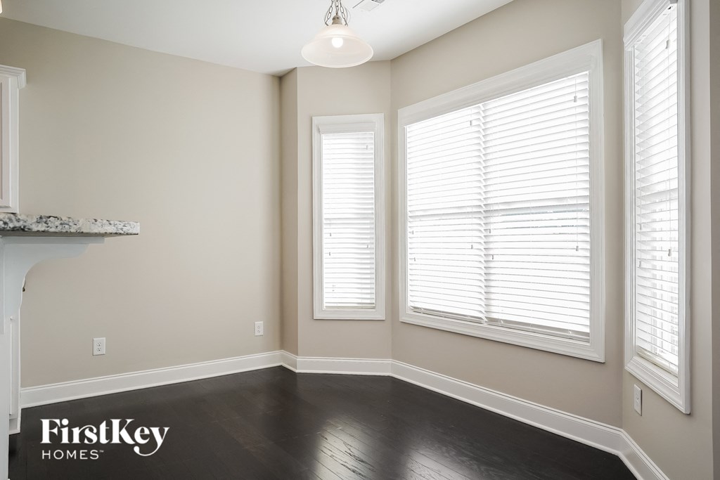 a living room with a large window with white blinds and a dark wood floor