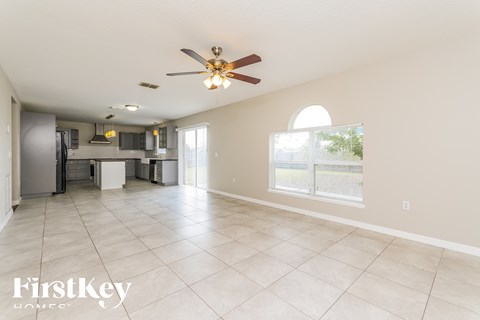 A spacious kitchen and living room with a ceiling fan and large windows.