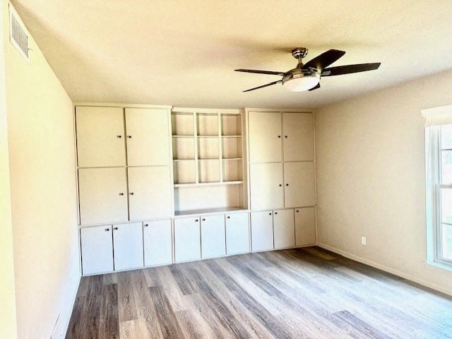 A room with a ceiling fan and built-in cabinets.
