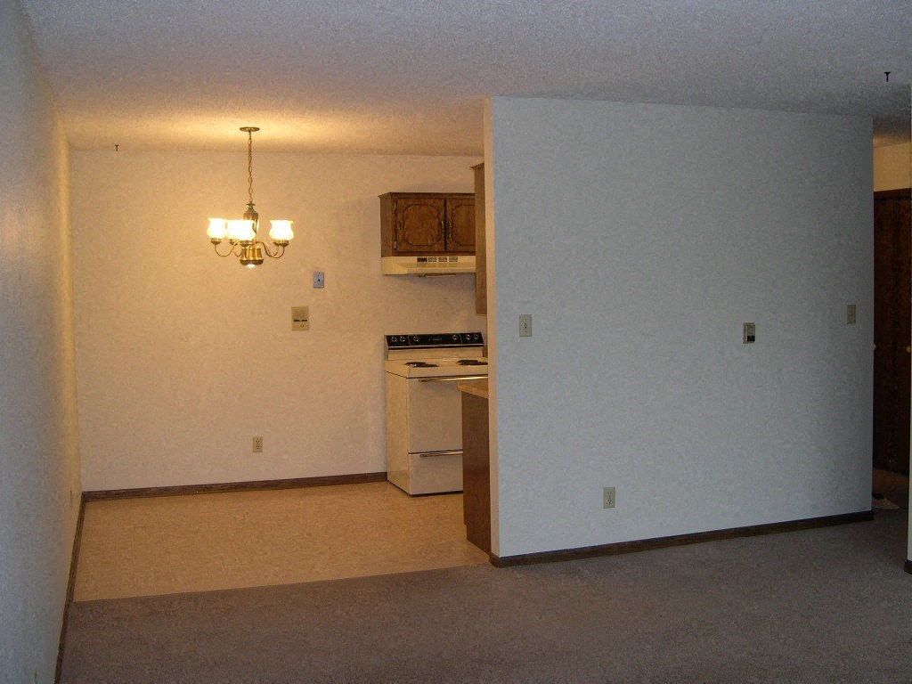 an empty living room with a stove and a kitchen