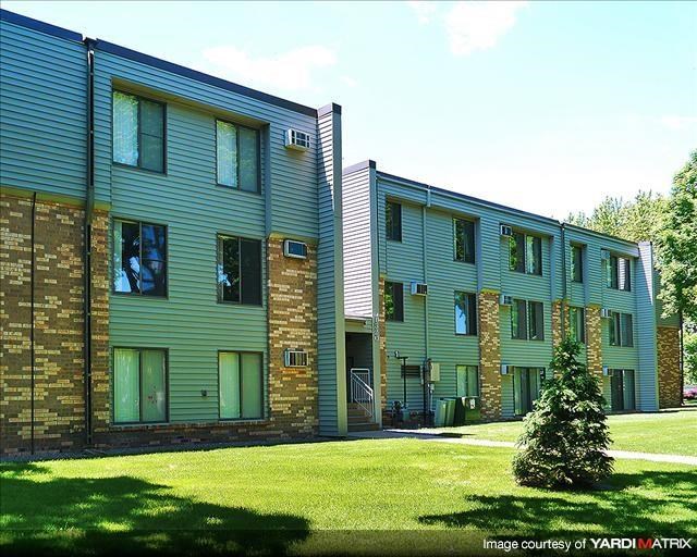 a green apartment building with a small tree in the yard