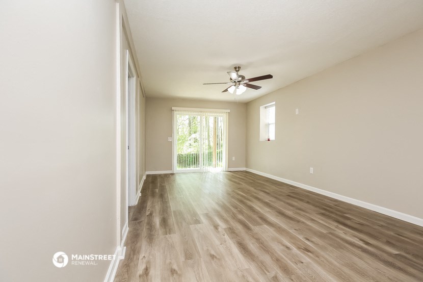 the spacious living room with hardwood flooring and a ceiling fan