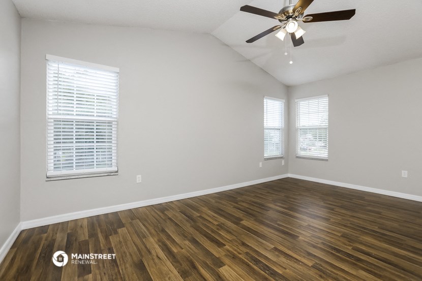 the spacious living room with wood flooring and a ceiling fan