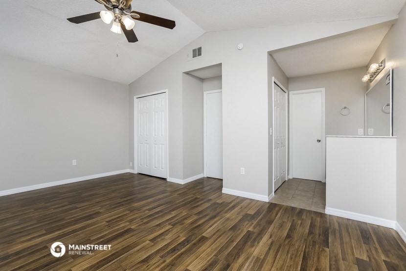 the spacious living room with white walls and wood flooring and a ceiling fan