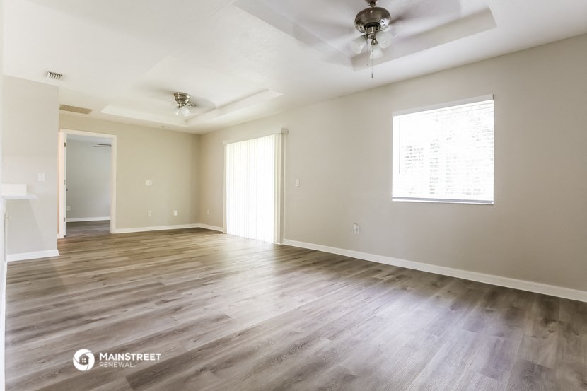 the spacious living room with wood flooring and a ceiling fan