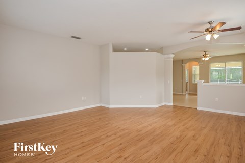 the spacious living room with hardwood flooring and a ceiling fan