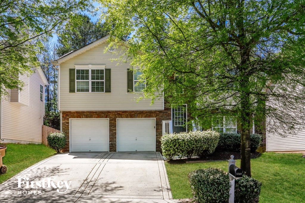 a white house with two garage doors in front of a tree