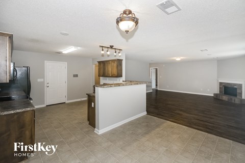 A well-lit, empty living room with a fireplace and a kitchen area in the background.