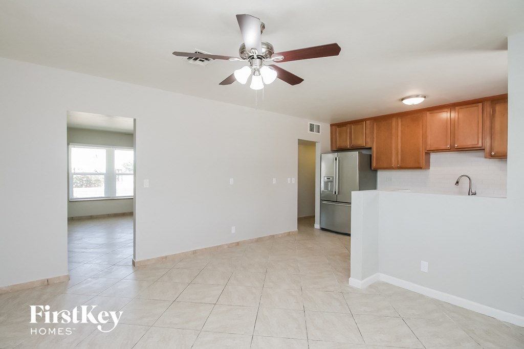A spacious room with a ceiling fan and a kitchen area with wooden cabinets.