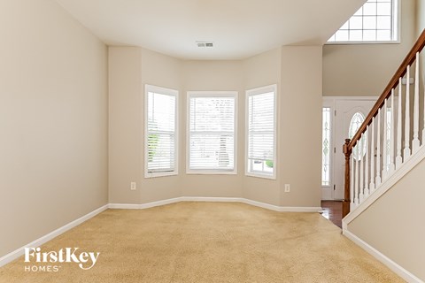 A spacious room with a carpeted floor and a staircase on the right side.