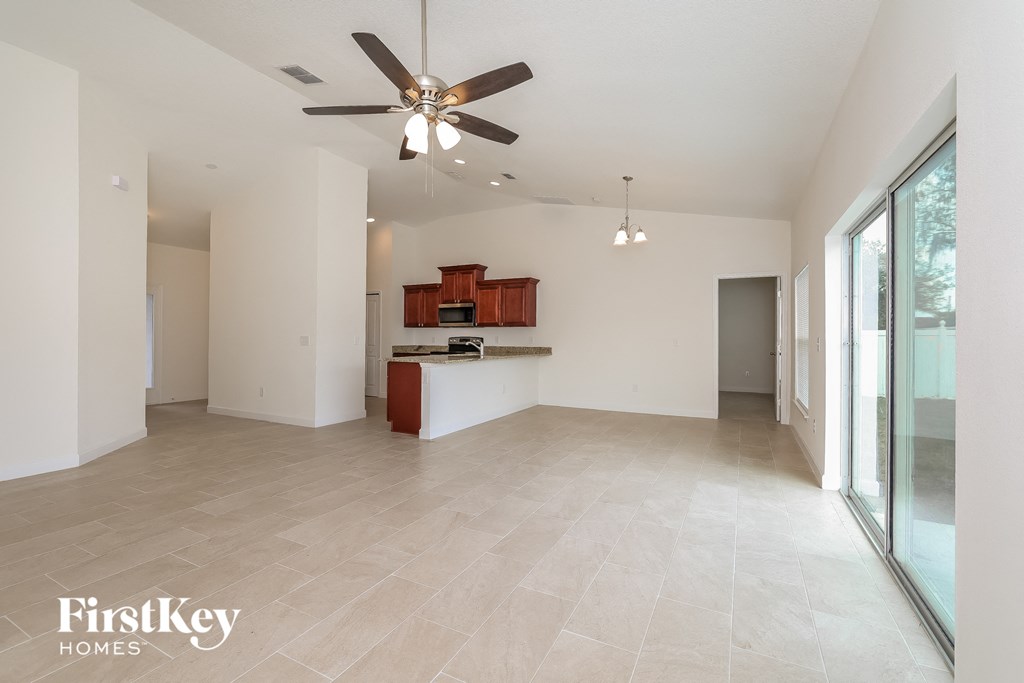 A spacious living room with a ceiling fan and a kitchen area in the background.