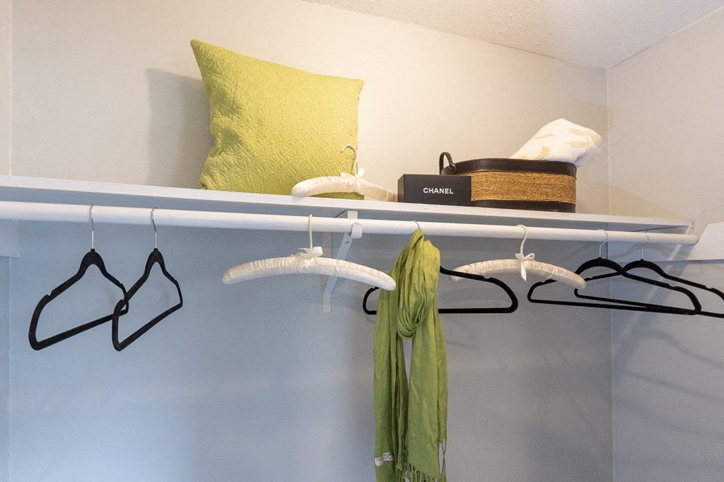a closet with glasses and a pillow and a green dress on a shelf