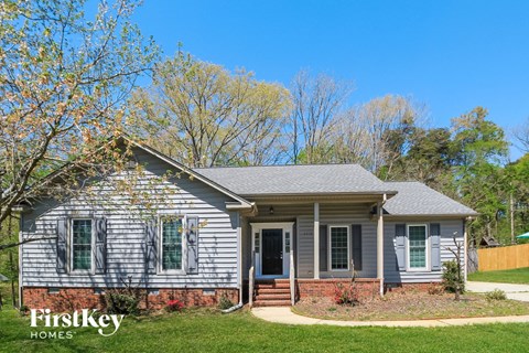 front view of a white house with green shutters and a lawn and trees