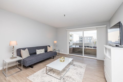 A living room with a grey couch, a white coffee table, and a television on a white cabinet.