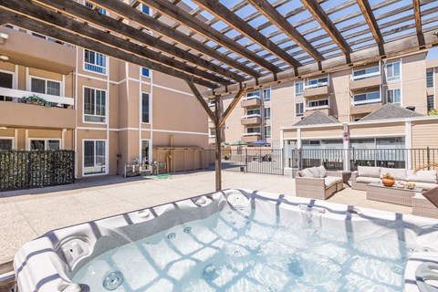 A hot tub is in the middle of a patio with a wooden pergola above it.