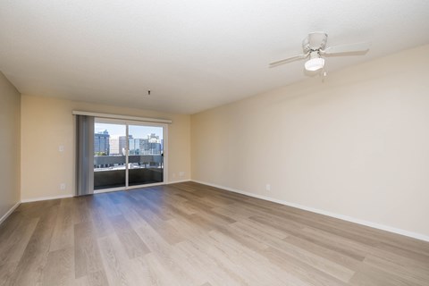 A room with a ceiling fan and a view of the city through a sliding glass door.