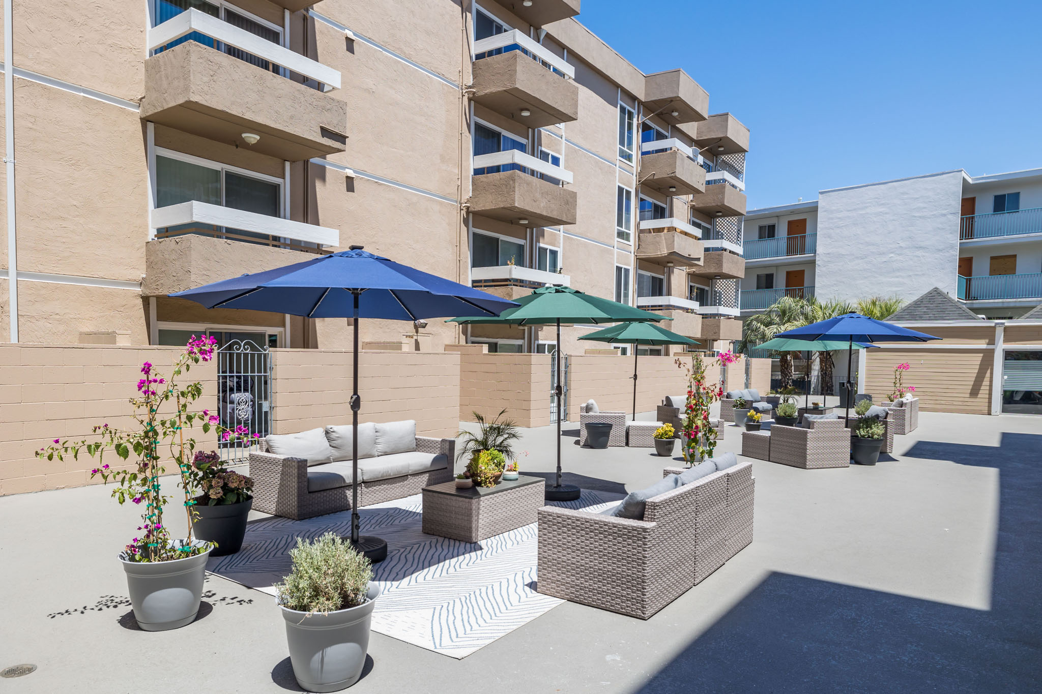 A patio area with a white couch, green umbrella, and potted plants.