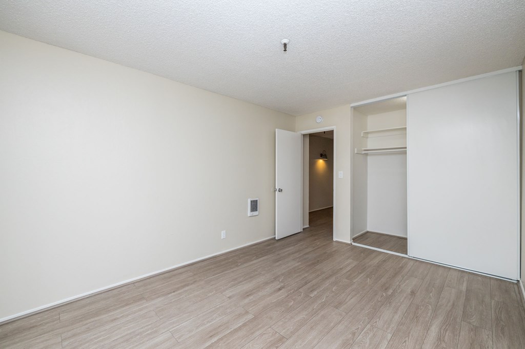 the living room and dining room of an apartment with wood flooring and white walls