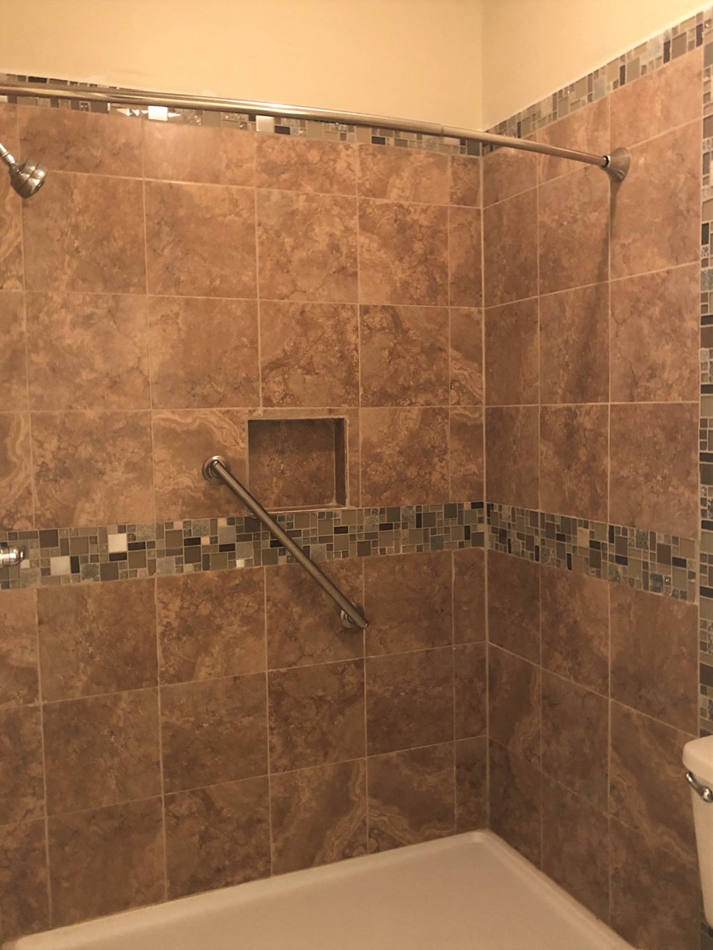 a tiled shower with a grab rail in a bathroom