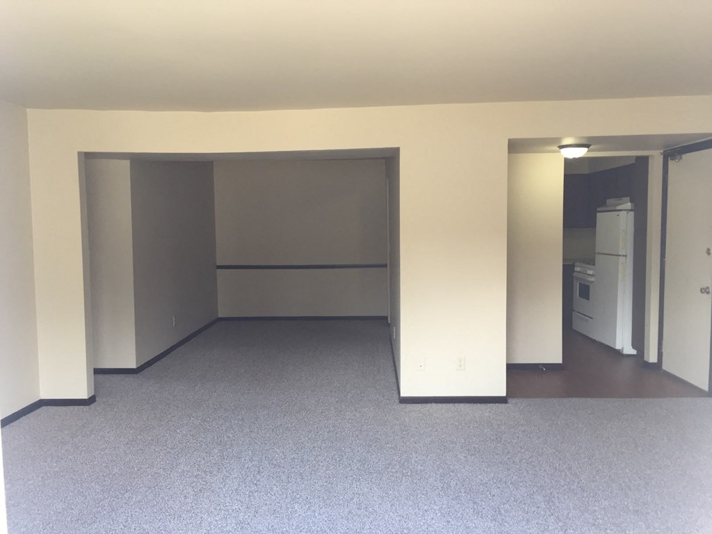 an empty living room with open doors and a kitchen