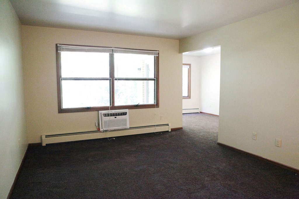 an empty living room with a window and a air conditioner