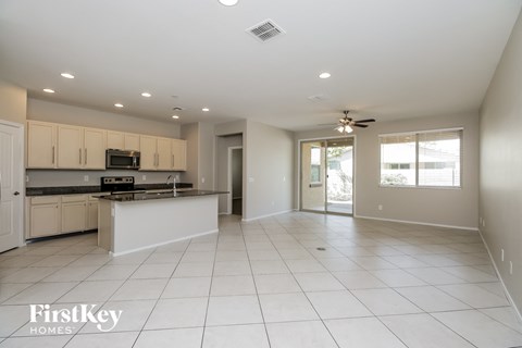 A spacious kitchen and living room with white tile flooring and a ceiling fan.