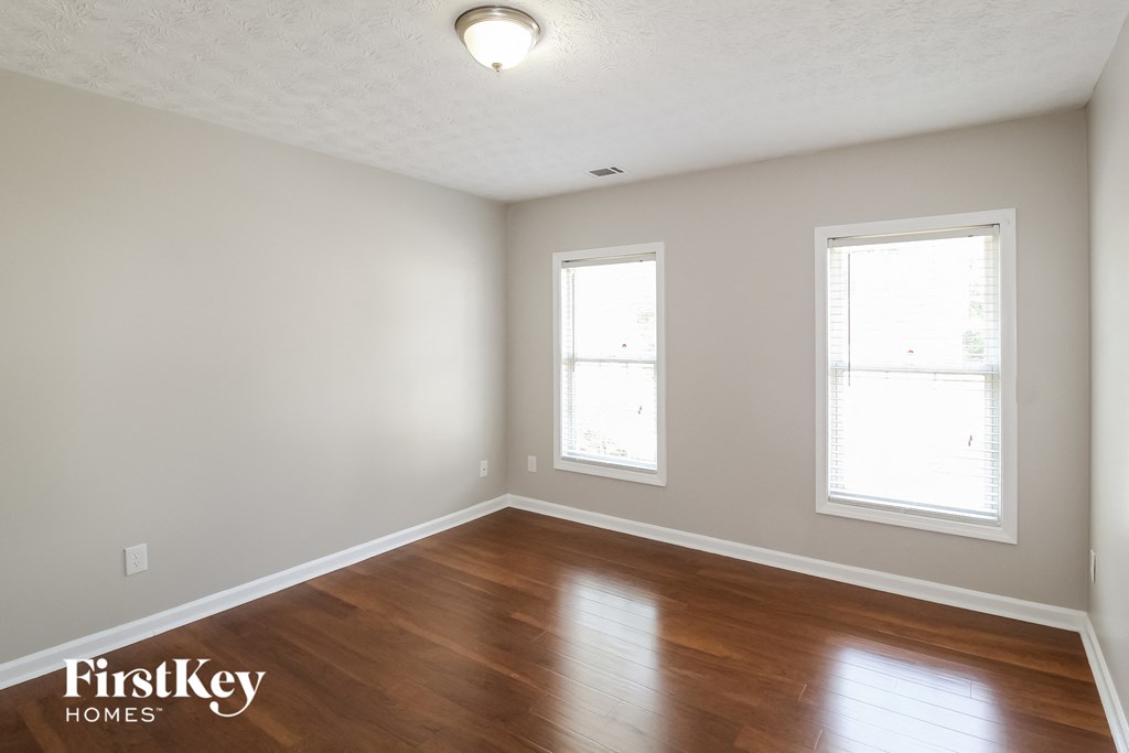an empty room with wood floors and two windows