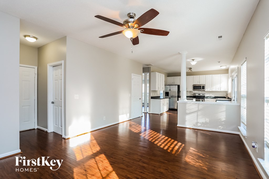 A spacious living room with a ceiling fan and wooden floors.