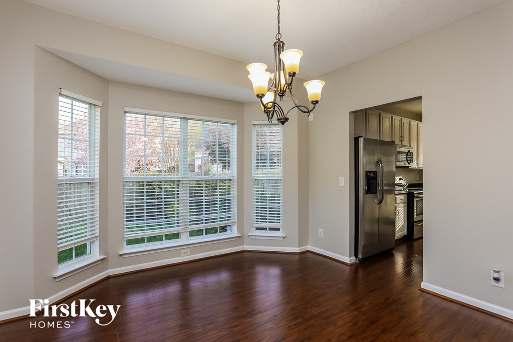 A large empty room with a chandelier and a kitchen in the background.