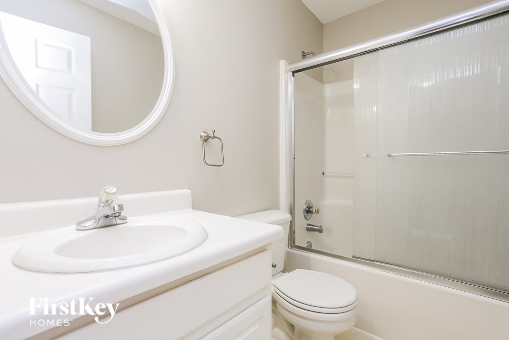A white bathroom with a round mirror and a glass shower door.