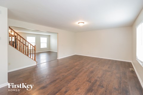 A spacious room with wooden flooring and a staircase on the left side.
