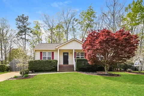 A house with a red door and a tree with red leaves in front.