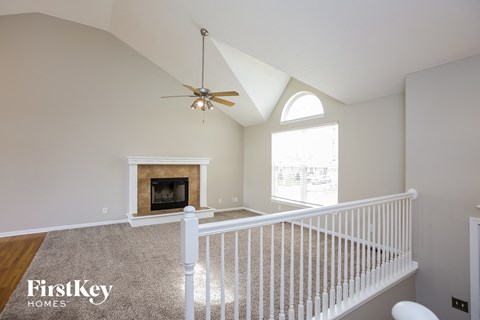 a landing with a white railing and a ceiling fan and a fireplace
